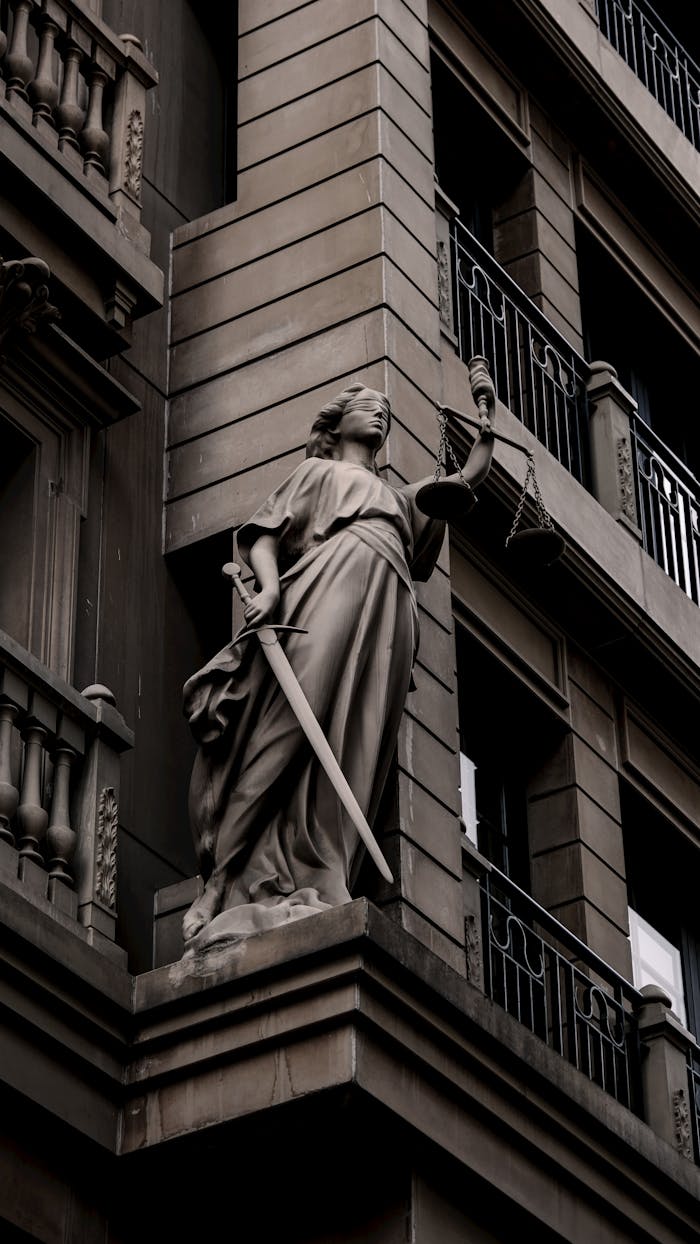 journey A sculpture of Lady Justice with a sword and scales on a city building's facade.