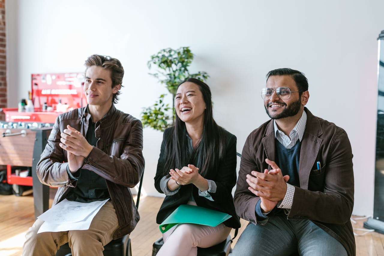 services-01 Three diverse team members clapping and smiling during an indoor meeting, showing positivity and teamwork.